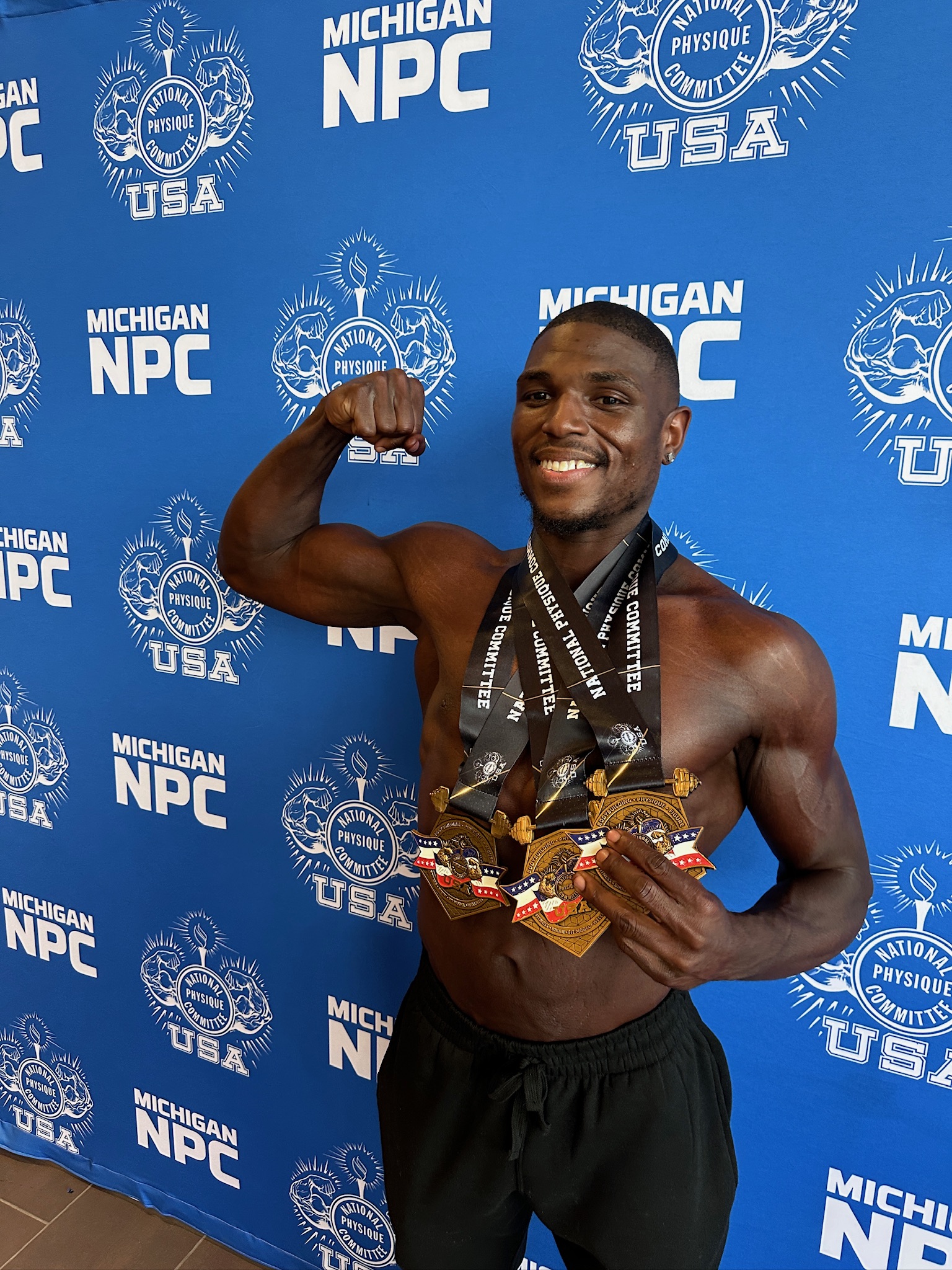 Andre backstage with medals, flexing right bicep and smiling