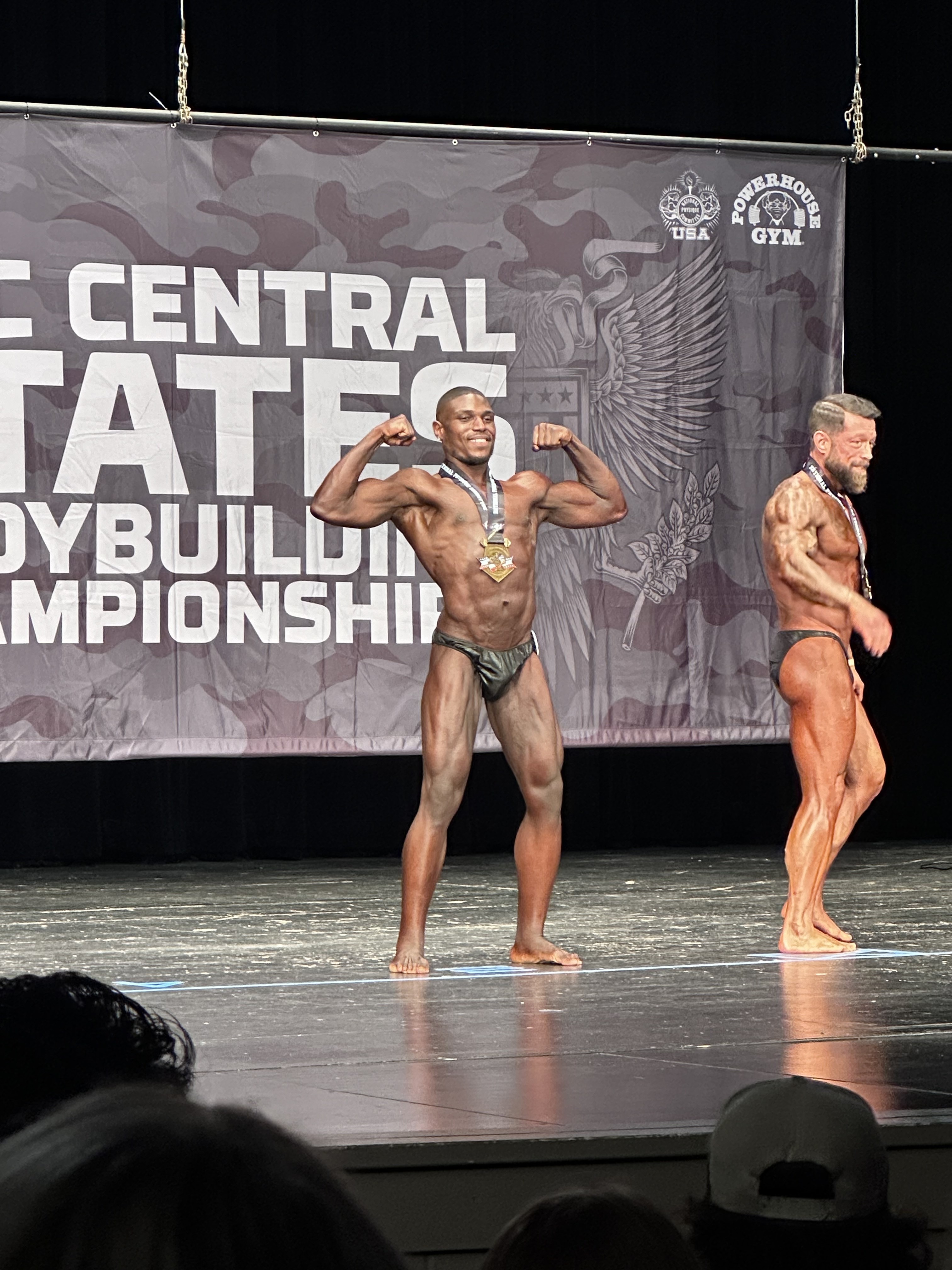 Andre flexing on stage with competitor